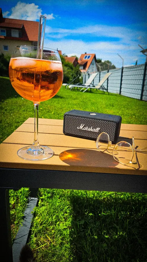 A summer drink on a garden table, the sunny lawn and fence behind